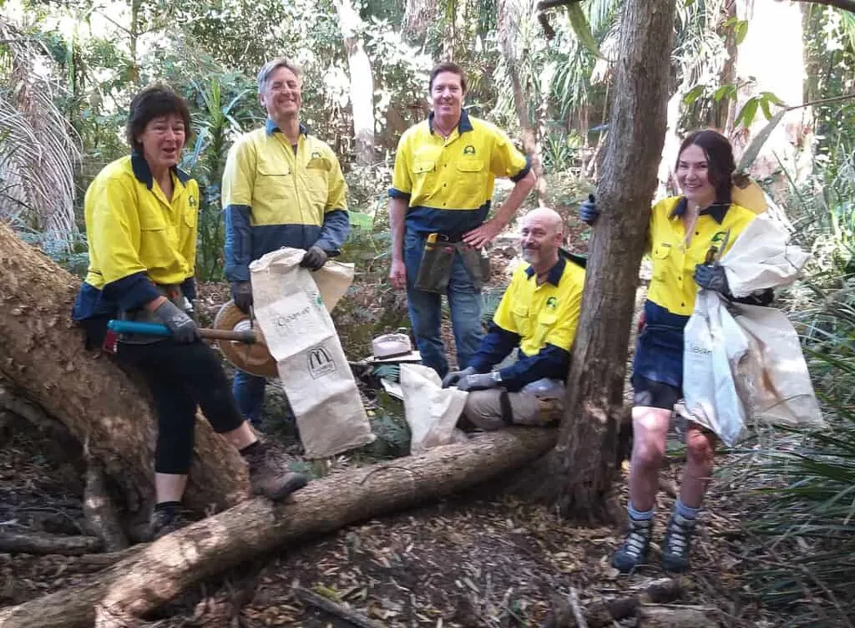 Landcare volunteers in hi-vis shirts and hats sitting and chatting on a nature strip after a working bee